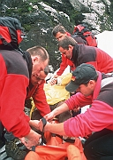 Ratownicy TOPR pakuja rannego turyste do noszy, przygotowanie do transportu.